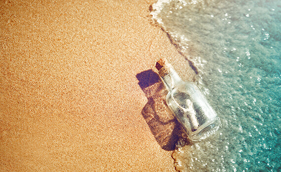A bottle with a message is thrown by a wave on a sandy beach. Soft wave of blue ocean on sandy beach. The bottle floats in the surf line CET10