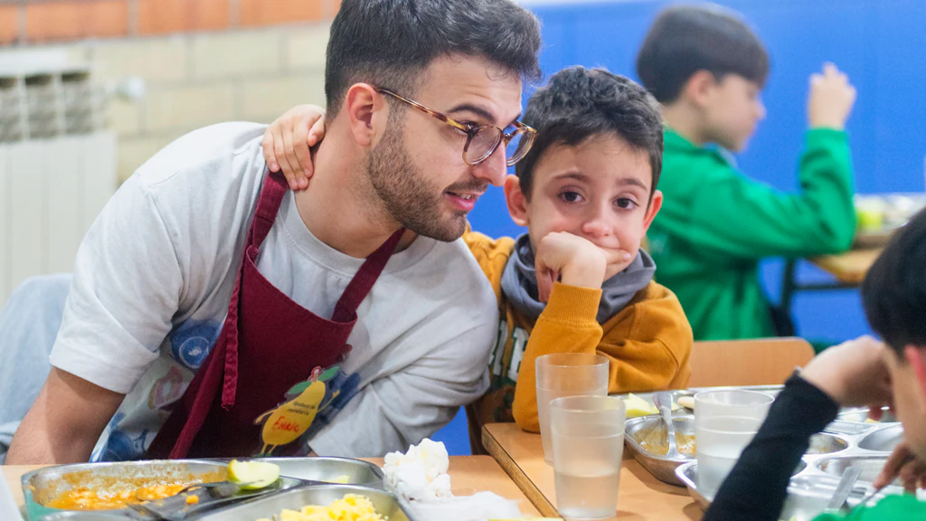 Monitor acompanyant a un nen en un menjador escolar
