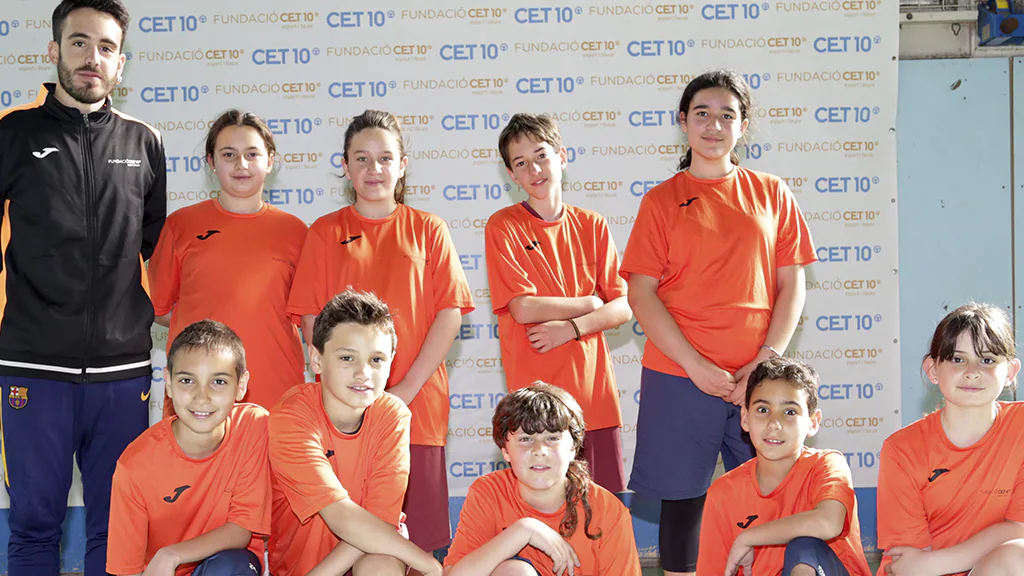 Equip de bàsquet amb el seu entrenador posant per a una foto amb un photocall de fons